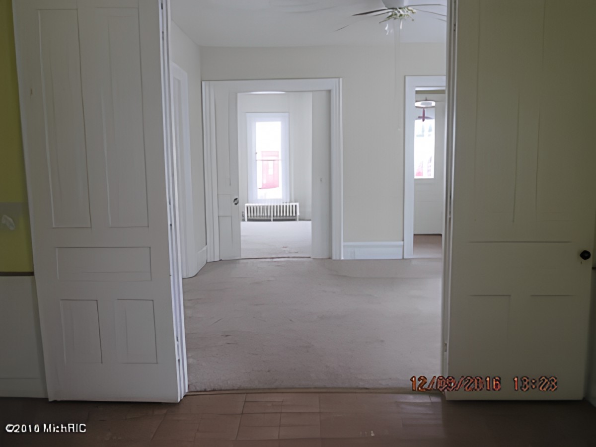 An empty room with a view through doorways, featuring carpeted floors and windows providing natural light.