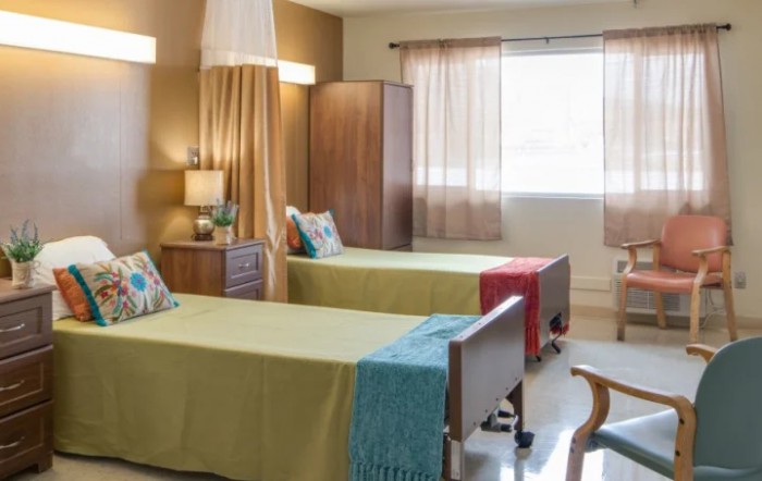 A well-lit hospital room with twin beds, colorful pillows, and cozy decor.