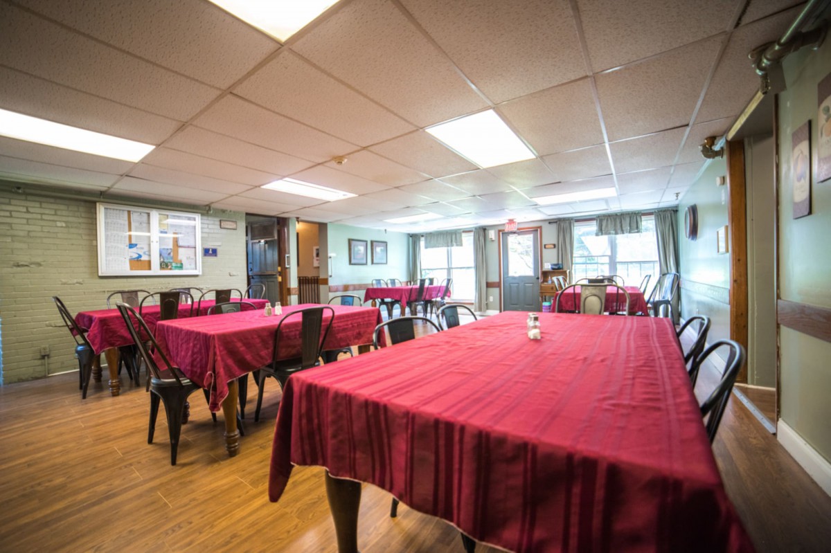 A cozy restaurant dining area featuring tables with red tablecloths and ample natural light.