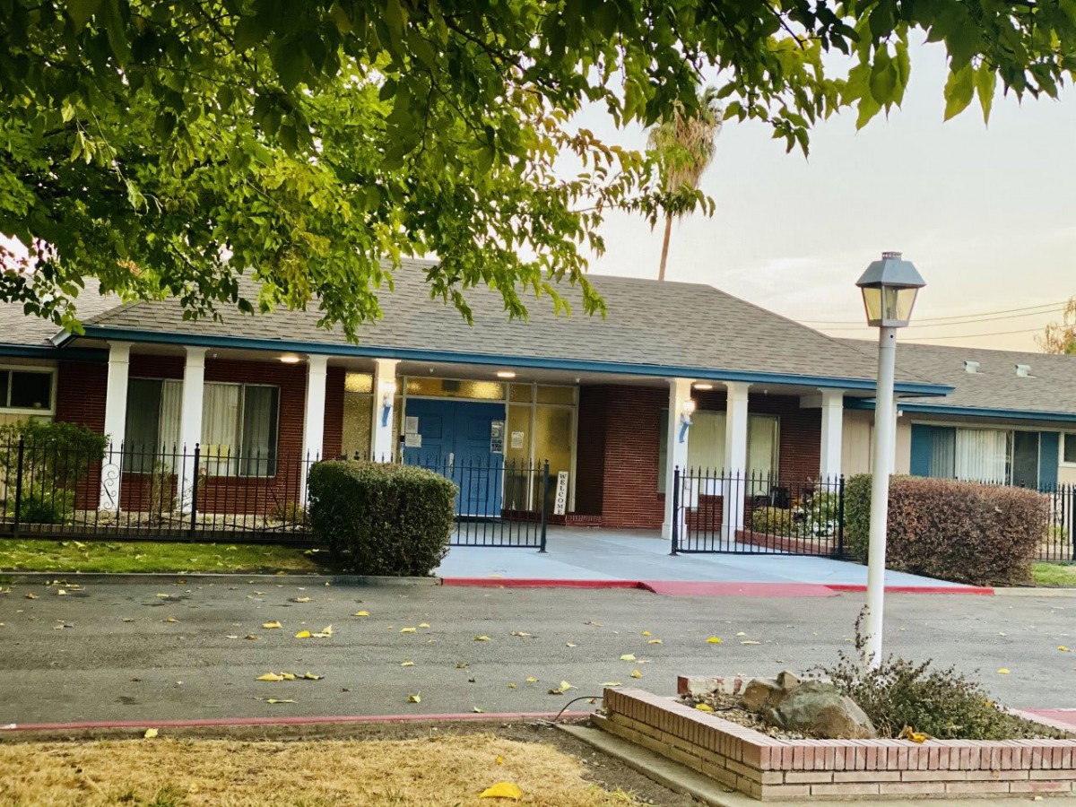 A small building with a blue door and white pillars, surrounded by trees and a parking area.