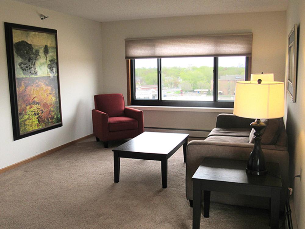 A cozy living room with a sofa, armchair, coffee table, and a large window providing natural light.