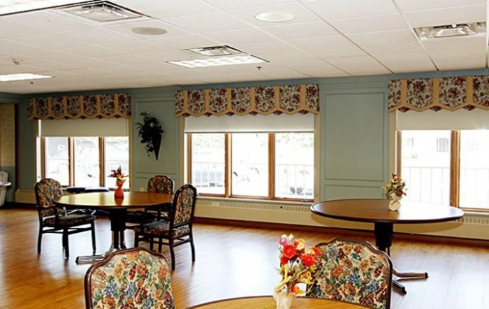 A bright dining area with tables, chairs, and floral-patterned decor near large windows.