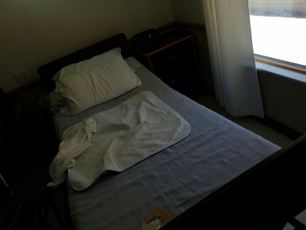 A messy bed in a dimly lit bedroom with a window nearby.