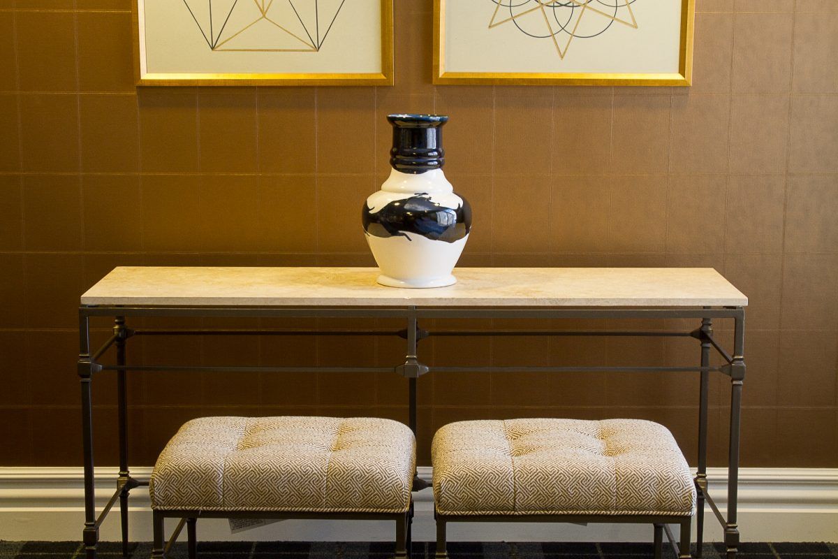 A modern interior featuring a console table with a black and white vase, flanked by two upholstered stools under framed geometric artwork.