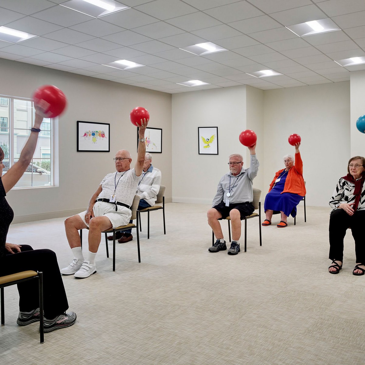 A group of seniors participating in an indoor exercise class using red balls.