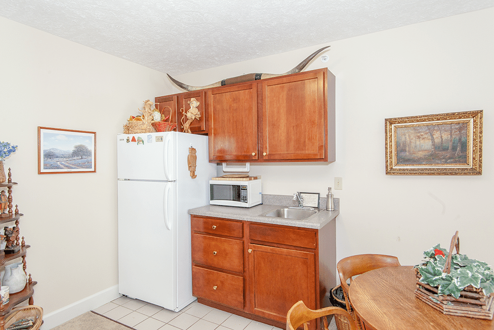 A small kitchen area with wooden cabinets, a refrigerator, and a microwave, adorned with decorative antlers.