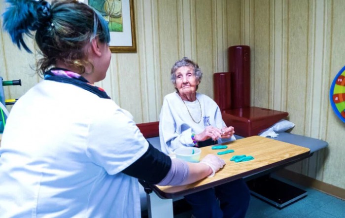 An elderly woman engages in a card game with her caregiver in a cozy indoor setting.