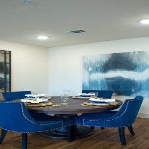 A modern dining room featuring a round wooden table surrounded by blue upholstered chairs and abstract artwork on the wall.