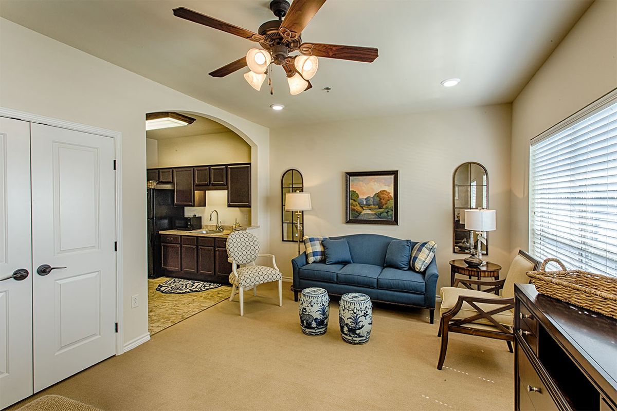 A cozy living room with a blue sofa and kitchen view, accentuated by elegant decor and a ceiling fan.