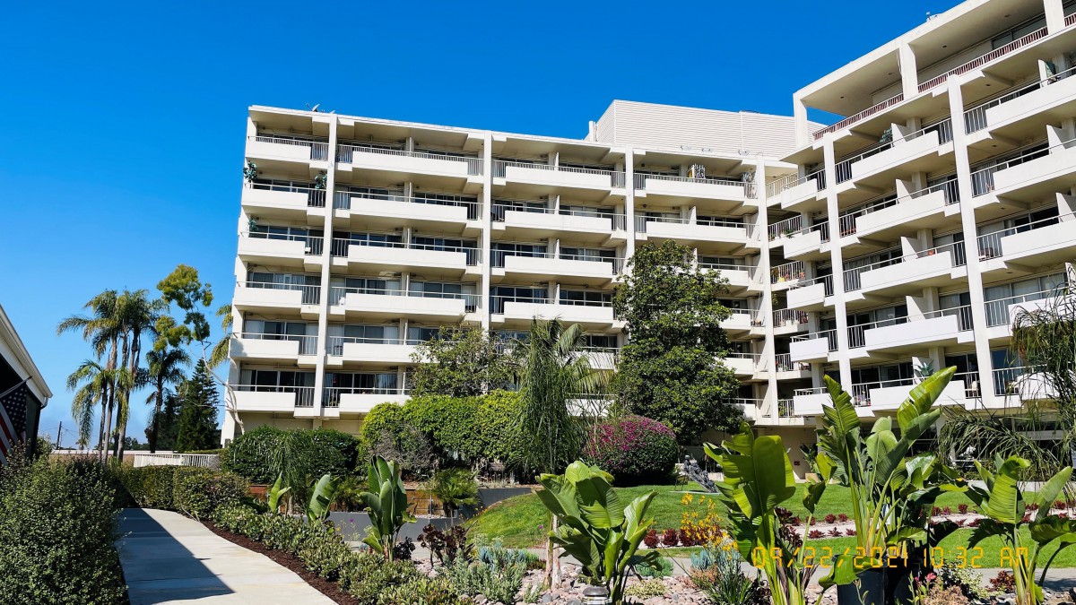 A residential apartment building with multiple balconies, surrounded by a landscaped garden and lush greenery.