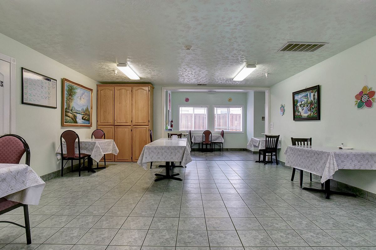 A spacious dining room with multiple tables and chairs, featuring tile flooring and paintings on the walls.