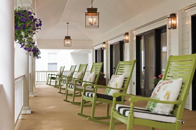 A cozy porch with green rocking chairs lined up by lanterns.