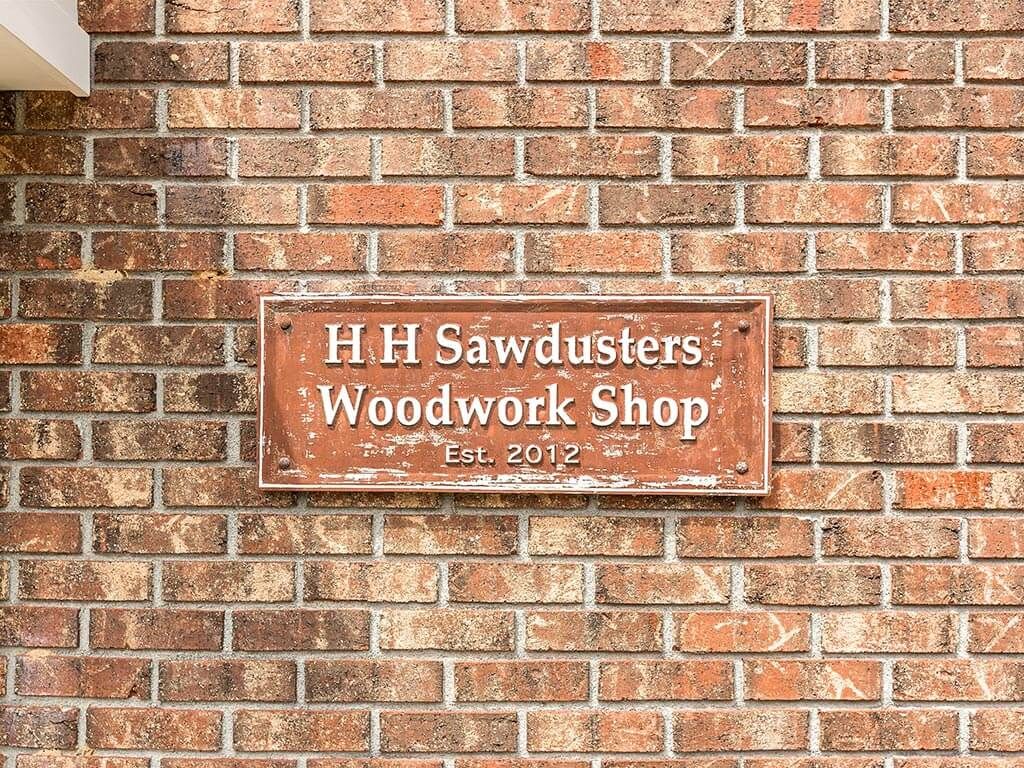 A vintage sign for 'H H Sawdusters Woodwork Shop' on a brick wall.