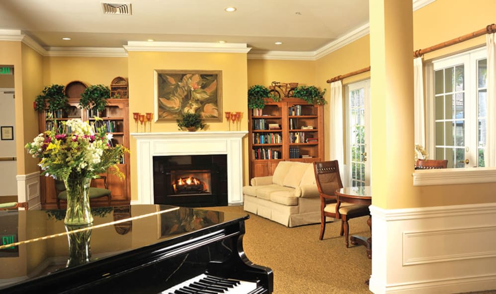 A cozy living room featuring a fireplace, bookshelves, and a grand piano.