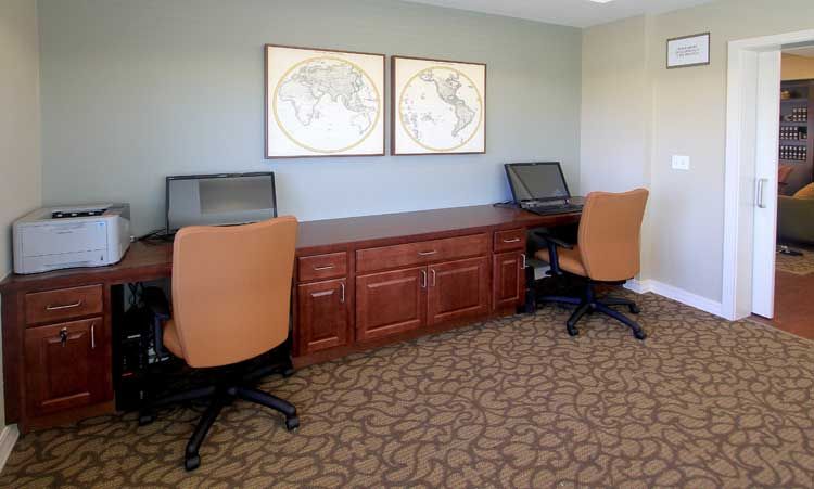 A neat office workspace featuring two computers on a long desk with brown chairs, and map art hanging above.