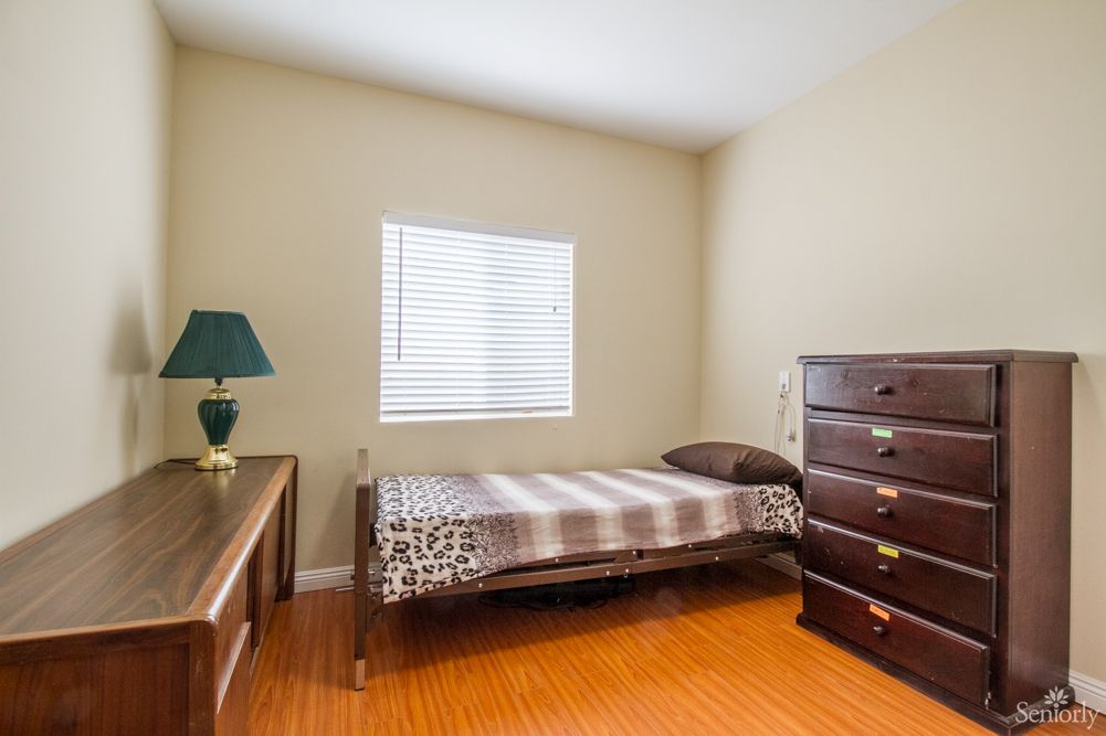 A cozy bedroom with a single bed, dresser, and desk, featuring a window with blinds.