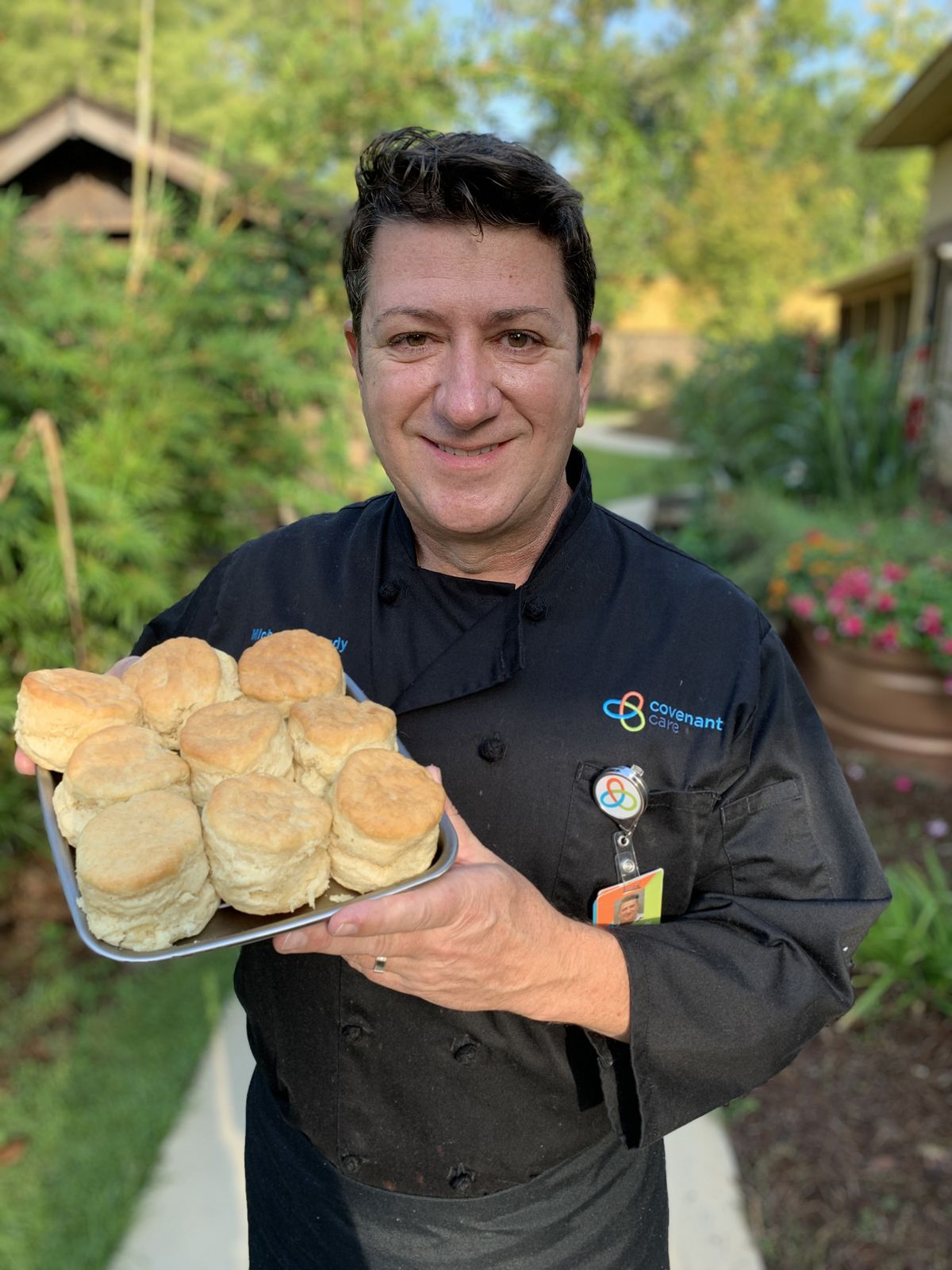 Chef proudly presenting a tray of freshly baked biscuits outdoors.