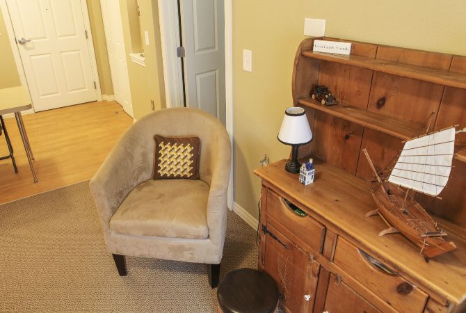 A cozy corner with a beige chair and a wooden desk featuring a lamp and decorative items.
