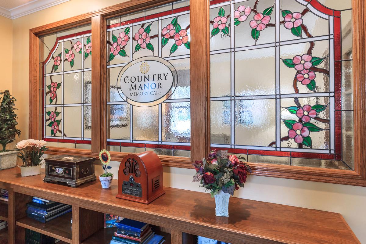 A cozy interior with a decorative stained glass window, featuring floral designs and a wooden bookshelf adorned with an antique radio and a flower vase.