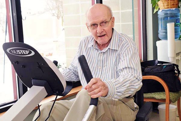An elderly man exercising on a stationary bike indoors.