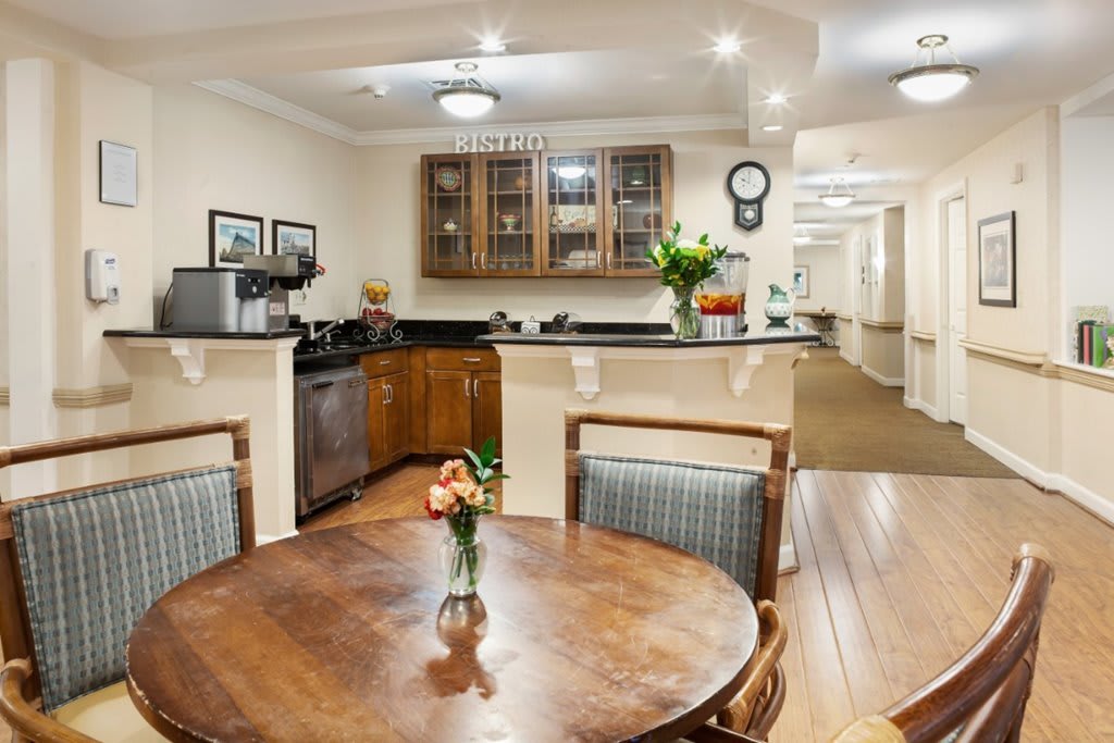 A cozy kitchen and dining area featuring a wooden table with chairs, surrounded by cabinets and adorned with flowers.