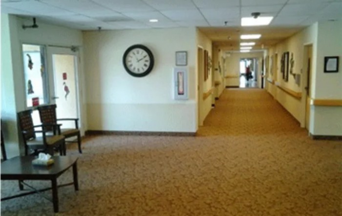 A carpeted hallway with a clock and chairs along the wall.
