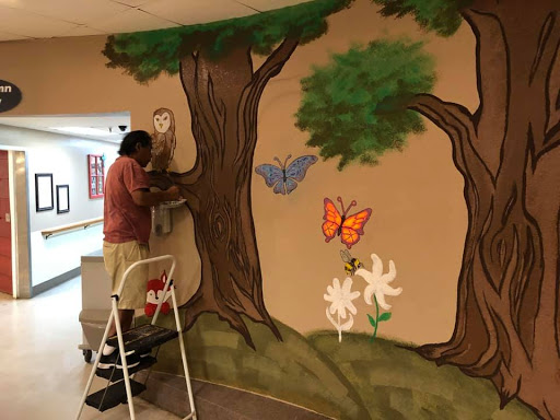 An artist adds finishing touches to a vibrant mural featuring trees, butterflies, and flowers.