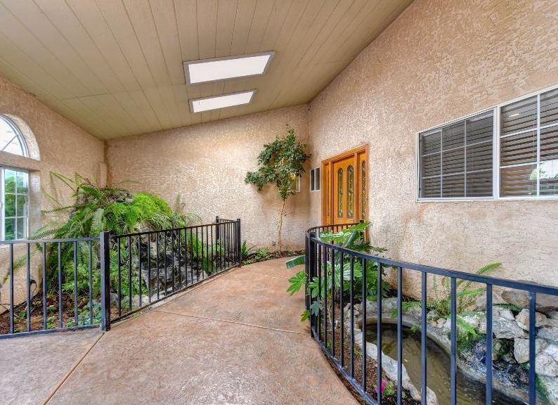 A peaceful indoor atrium featuring a walkway surrounded by lush plants and a small pond, illuminated by natural light from skylights.