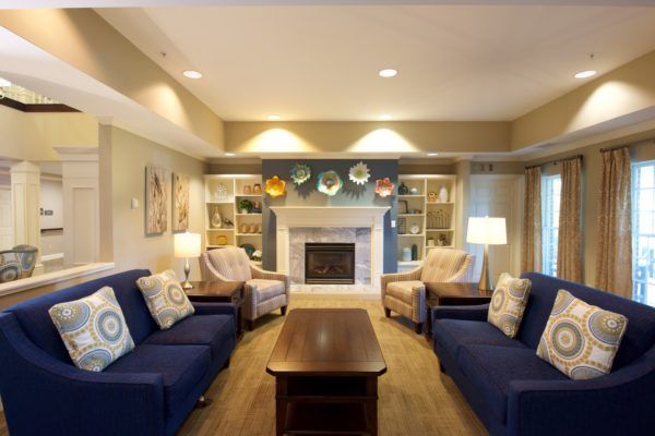 A cozy living room with a fireplace, flanked by blue sofas and armchairs, and highlighted with decorative plates on shelves.