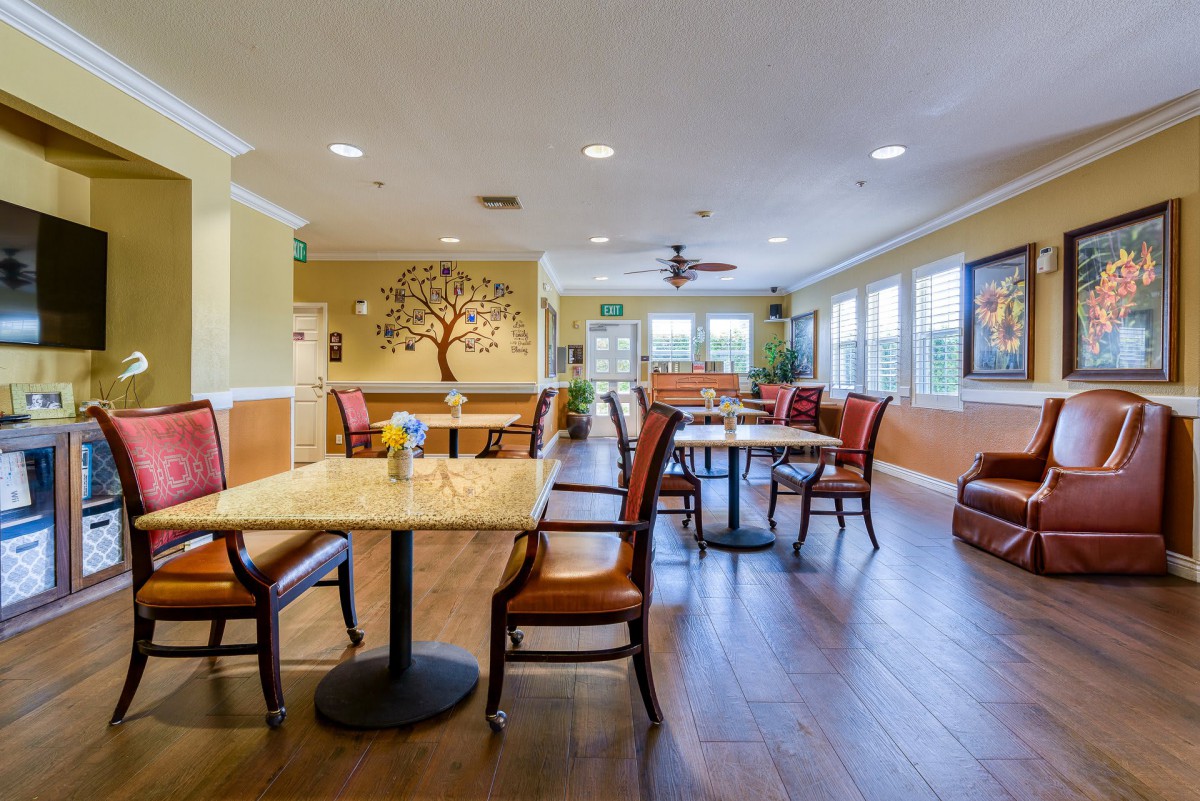 A well-lit dining room with neatly arranged tables and chairs, featuring warm decor and hardwood flooring.