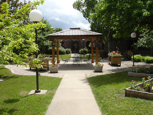 A serene garden featuring a wooden gazebo surrounded by lush greenery and a paved walkway.