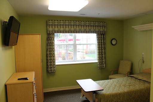 A well-lit room featuring green walls, a window with patterned curtains, and basic furniture.