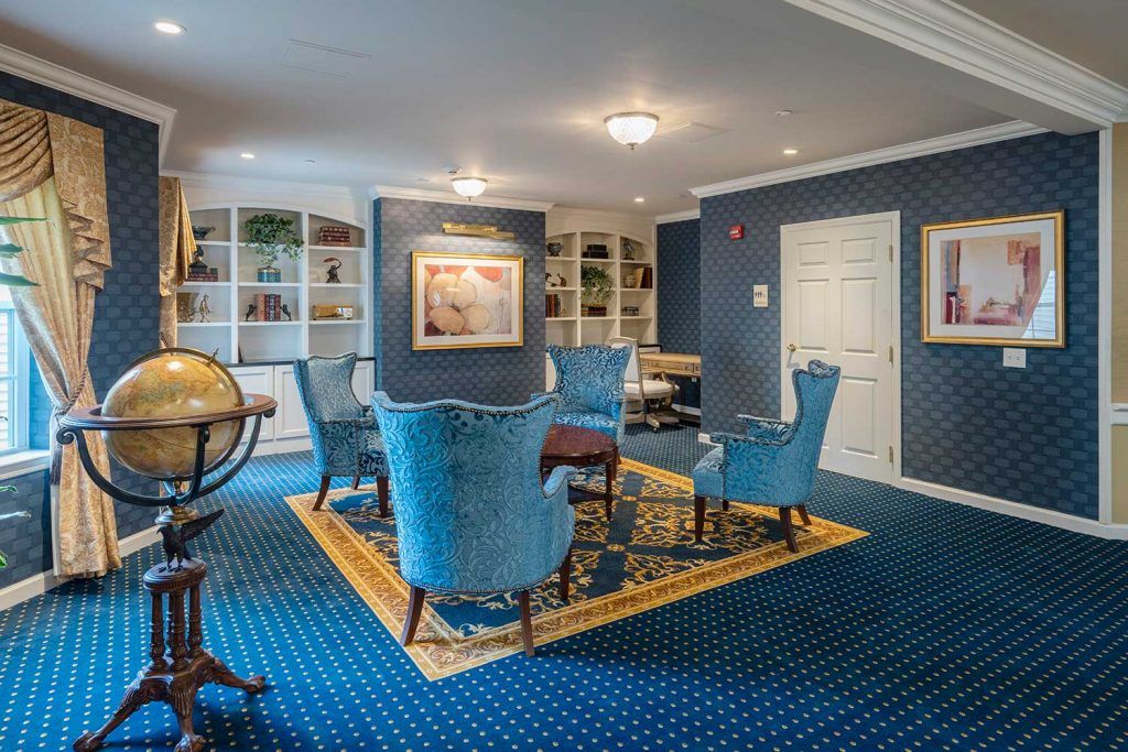 A cozy living room with elegant blue chairs and a carpeted floor, featuring bookshelves and wall art.