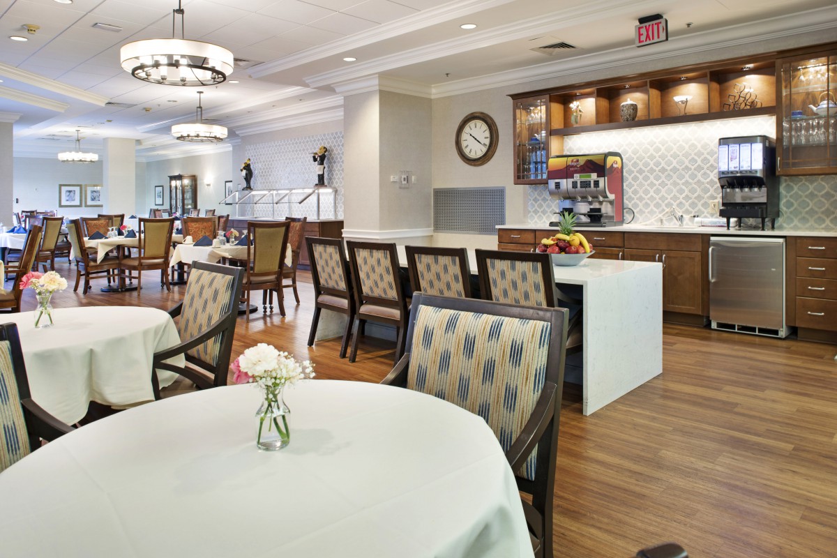 A modern dining area with elegantly set tables and chairs adjacent to a small kitchen space.