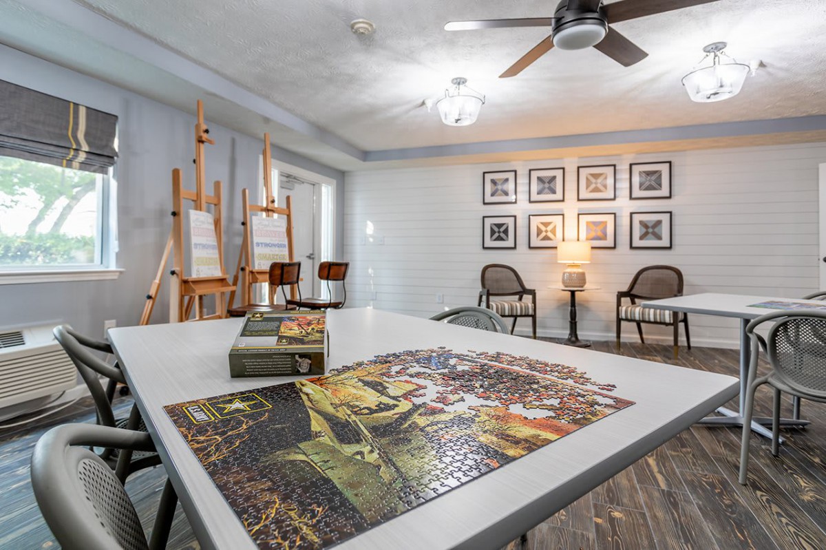 A cozy art studio featuring a puzzle on the table, surrounded by easels and framed art on the walls.