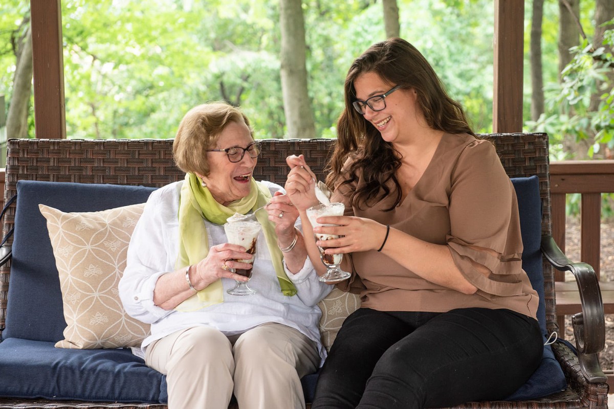 Two women enjoy ice cream together while sitting outdoors.
