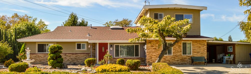 A suburban house with a manicured front yard under a sunny sky.