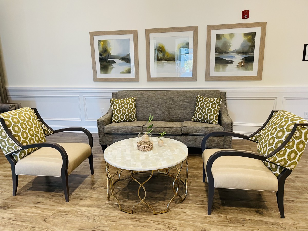 A cozy seating area with a gray sofa, two armchairs, and a round coffee table, adorned with nature-themed artwork on the wall.