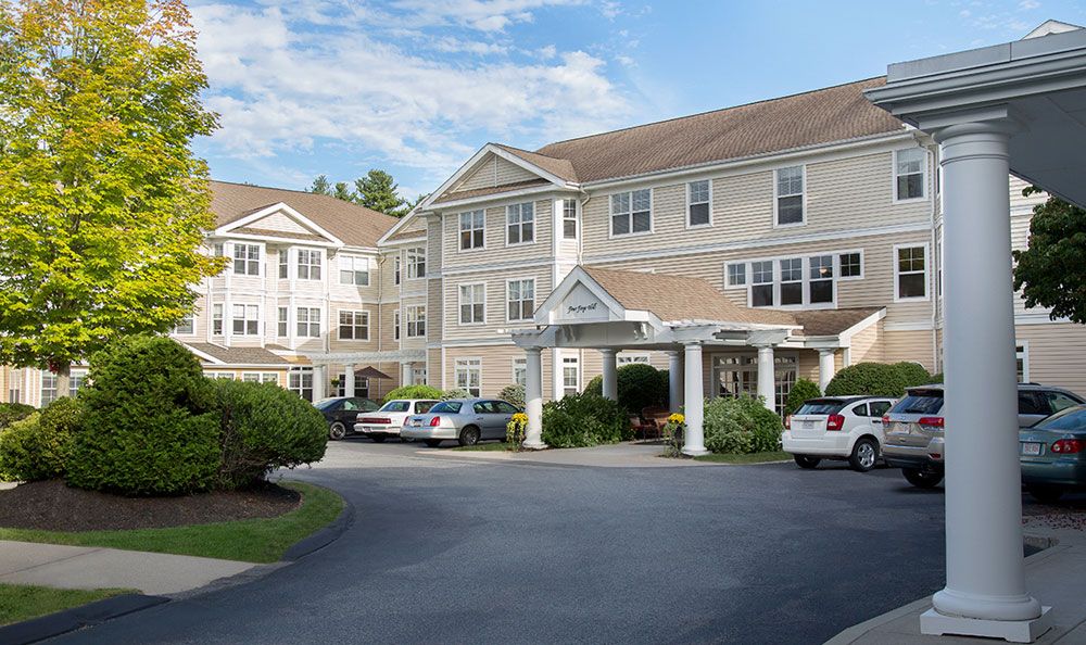 A view of a multi-story residential building with cars parked in the driveway.