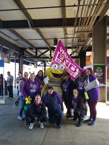Participants gather for a fundraising event, showcasing their support with vibrant purple attire and a cheerful mascot.