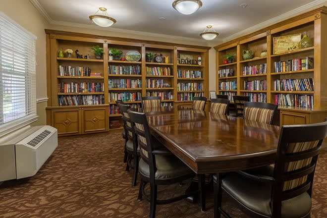 A well-furnished meeting room with a large conference table surrounded by chairs and lined with bookshelves filled with books.