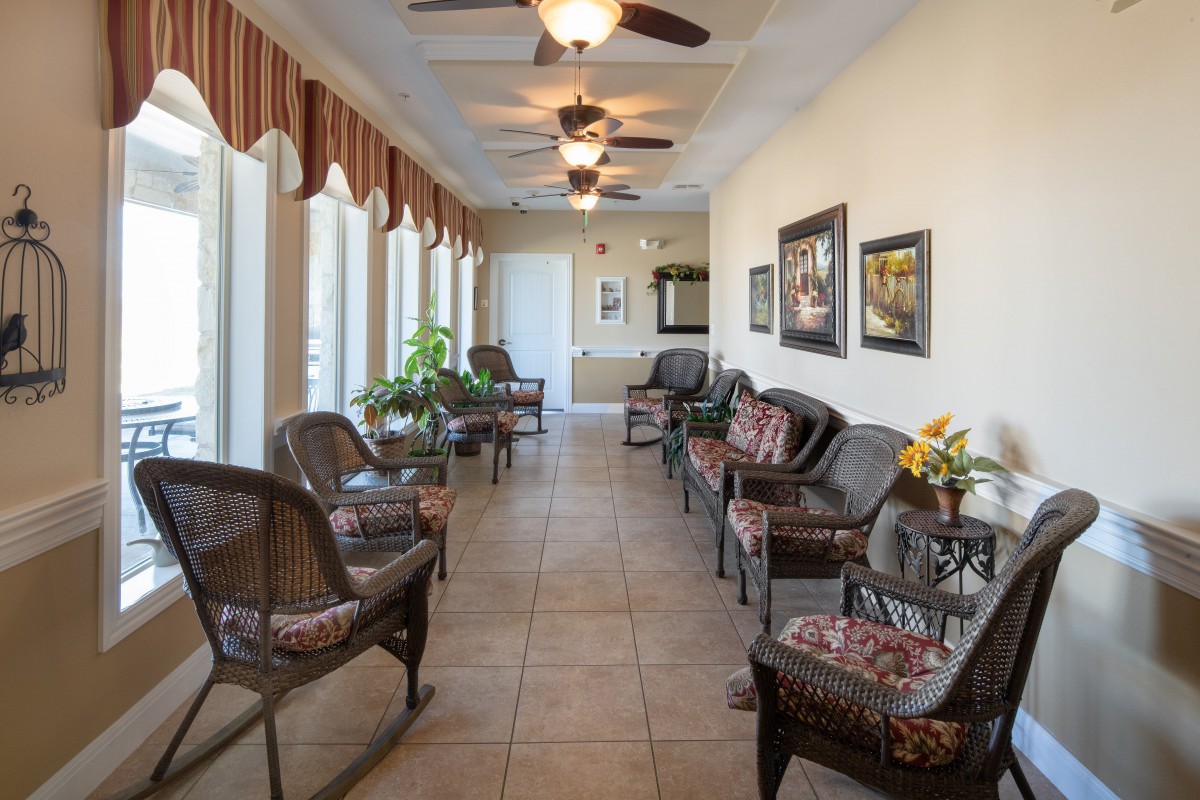 A well-lit waiting room featuring comfortable seating, ceiling fans, potted plants, and decorative artwork along the walls.