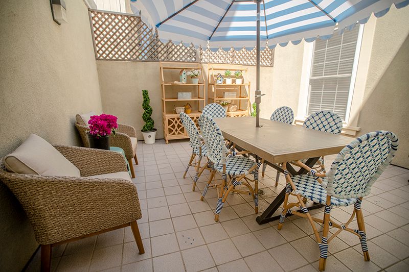 A cozy patio setup with a table and chairs under a striped umbrella, surrounded by plants.