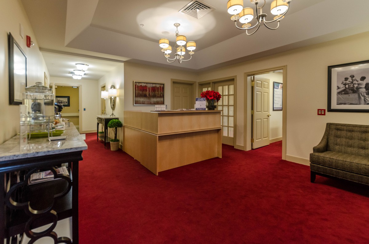 A well-lit reception area featuring a wooden desk, red carpet, and elegant lighting fixtures.