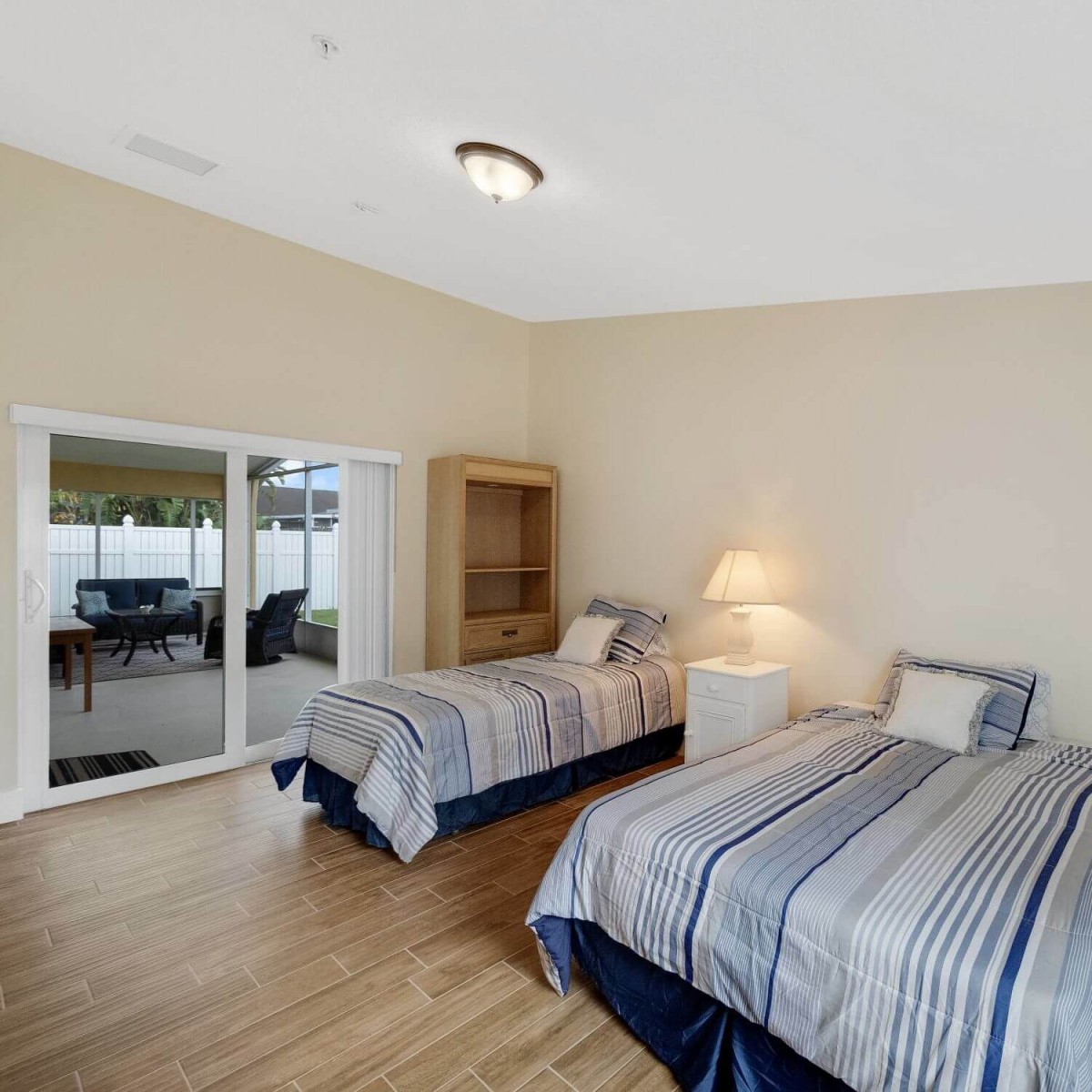 A minimalist bedroom with twin beds and wooden flooring, featuring a large window and simple furniture.