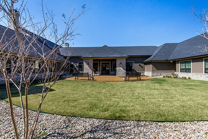 A well-maintained backyard showcasing a modern house with a wooden patio and spacious lawn.