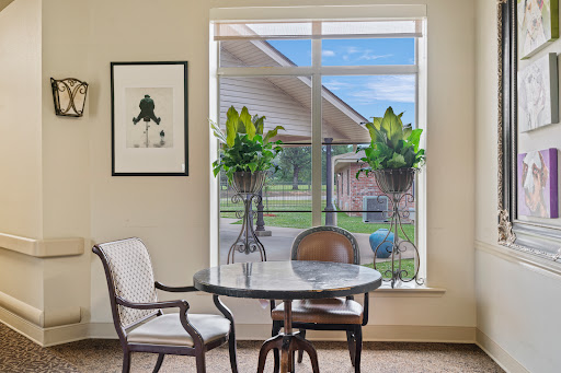 A cozy interior scene featuring a round table, stylish chairs, and vibrant plants by a large window.