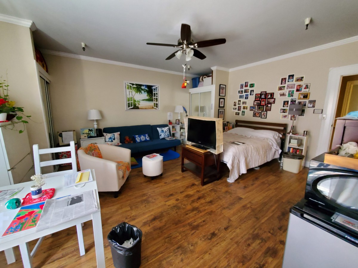A cozy studio apartment with a combination of living and sleeping areas, featuring a sofa, bed, and television on wooden flooring.