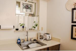 A small kitchen area with a sink, potted plants on the windowsill, and appliances like a coffee maker and toaster on the countertop.