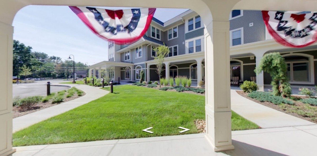 An exterior view of a modern apartment building with a well-maintained lawn and a patriotic banner hanging from the porch.